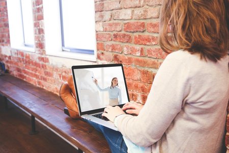 Frau sitzt auf einer Bank mit ihrem Laptop und verfolgt ein virtuelles Seminar