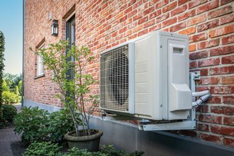 Luft-Luft-Wärmepumpe zur Kühlung oder Heizung des Hauses. Outdoor-Einheit mit erneuerbarer Energie, aufgehängt an einer Ziegelmauer Wand eines Einfamilienhauses.