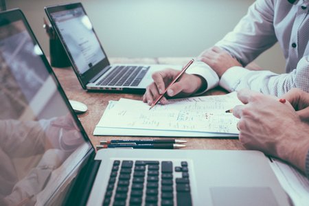 Arbeitstisch mit zwei Laptops und Papierunterlagen, Arme von zwei Personen bei der Arbeit sichtbar