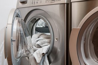 Silver washing machine and next to it a tumble dryer with the drum open and some washing hanging out.